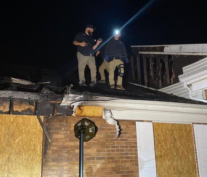 Construction Crew members on the roof of a burnt house, assessing & boarding up damage